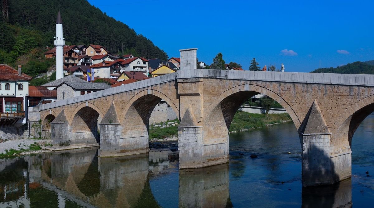 Old stone bridge over the river below a mosque in the Balkans